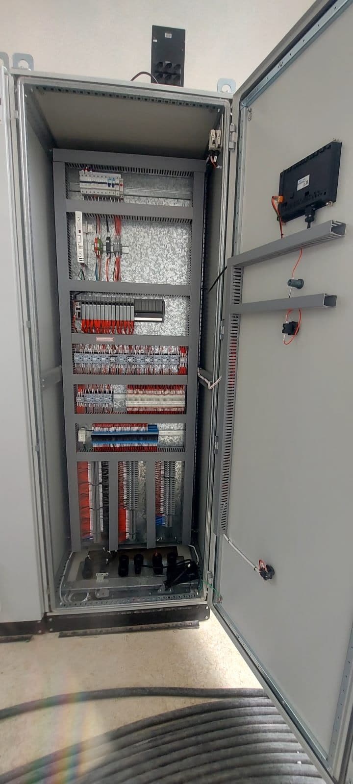Painel de comando e automação aberto, com rack de CLP, réguas de bornes com cabeamento identificado e IHM na porta